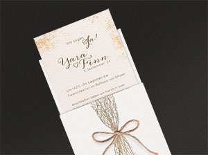 Einladungskarte zur BoHo-Hochzeit vor grauem Hintergrund liegend.