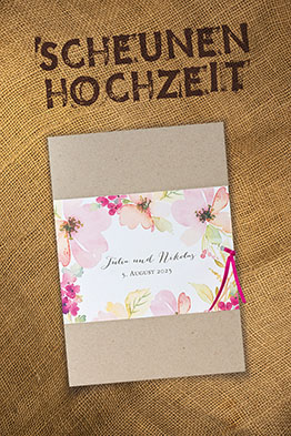 Hochzeitseinladungen aus braunem Kraftkarton, umgeben von einer weißen, mit Blumenaquarellen geschmückten Banderole.
