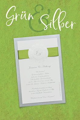 Weiße Hochzeitseinladungen, aufgeklebt auf silbernem, schillernden Trägerkarton, oben von einer grünen Schleife umfasst.