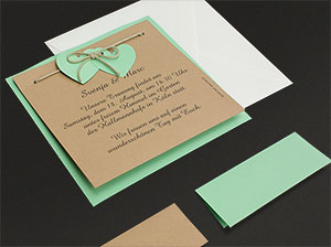 Hochzeitseinladungskarte, je eine grüne und weiße Tischkarte, sowie ein weißes Kuvert auf grauem Hintergrund liegend