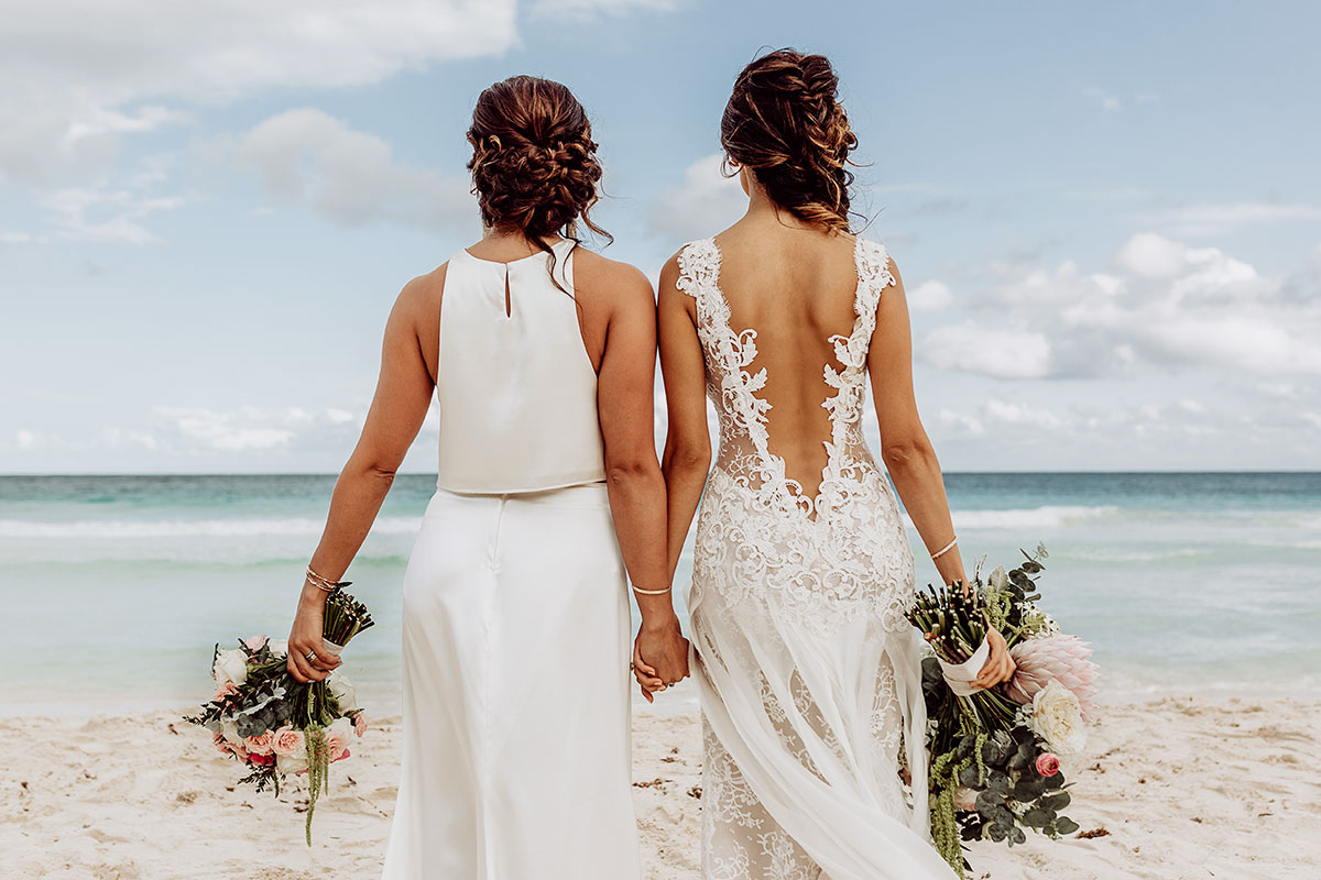 Regenbogenhochzeit. Braut und Braut Hand in Hand am Strand