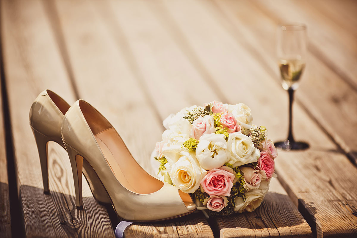 Hochzeitsschuhe, Brautstrauß und Sektglas auf  Holzboden.